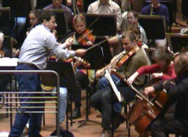 Terwijl de cellisten het in de hoogte zoeken, wordt de altsectie aangevuurd door dirigent Jules van Hessen.